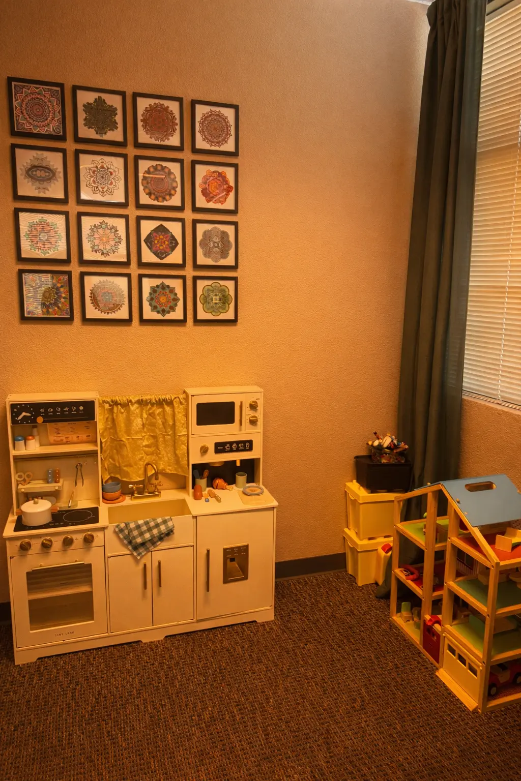 A bright play-therapy room with framed mandala tiles and a play kitchen